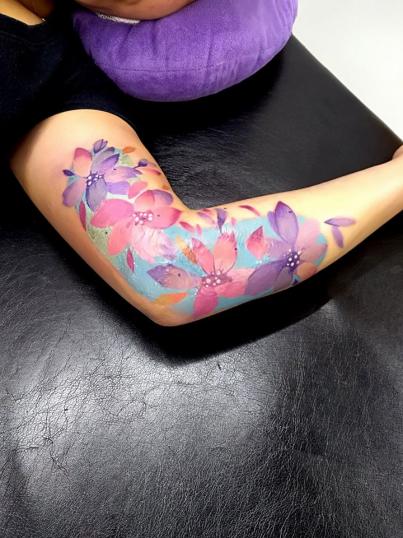 Flores de colores en el brazo tatuaje realizado por Adan dados uno