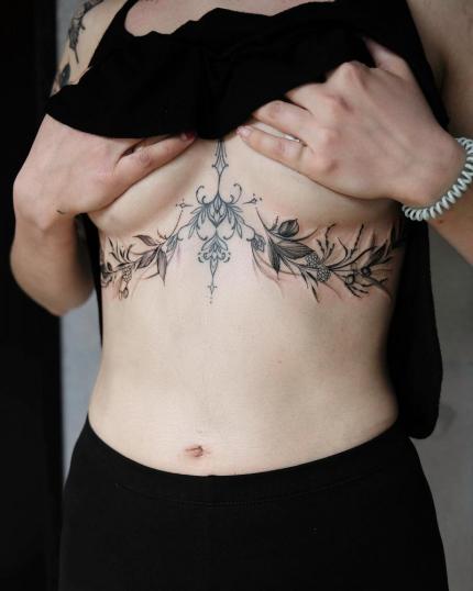 Tatuaje debajo del pecho con ornamentos y flores realizado por Stella Tattoo tatuaje realizado por Stella Tattoo